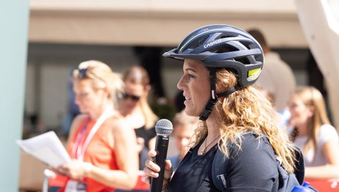 Manuela Stöckl mit Radhelm und Mikrofon bei einem Interview auf einer Radveranstaltung